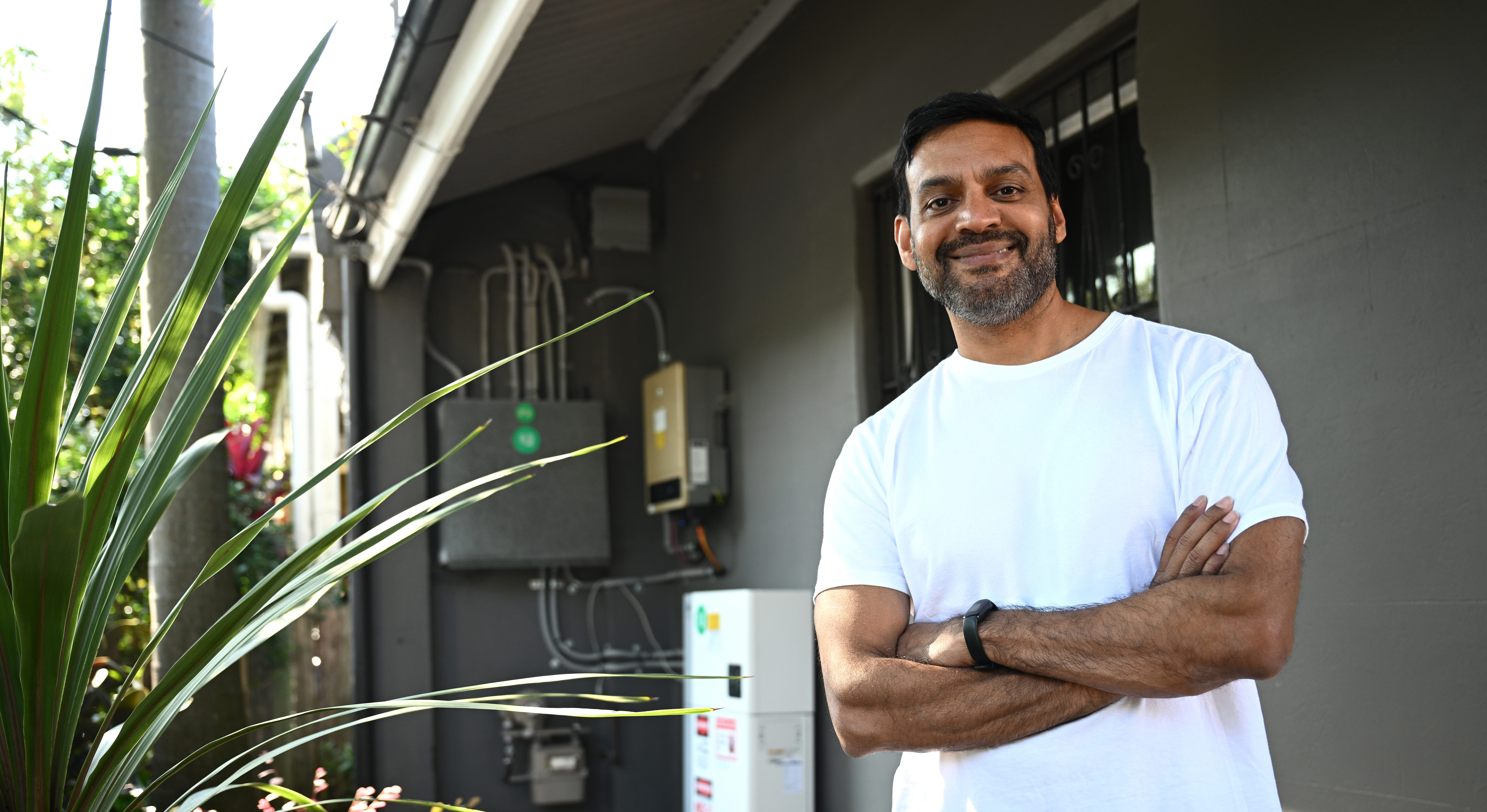 An image of Mamoon Reza, Sydney resident, standing out the front of his home with his home battery visible in the background.