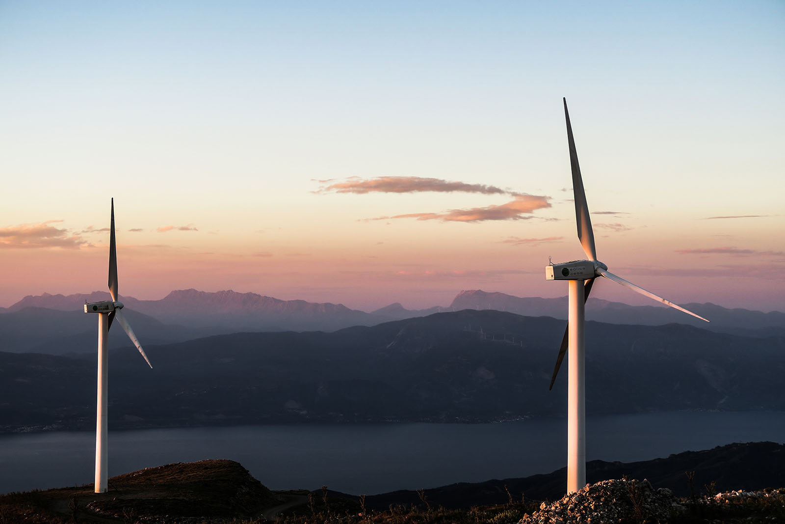 Photo of wind turbines at sunset in front of mountains and water